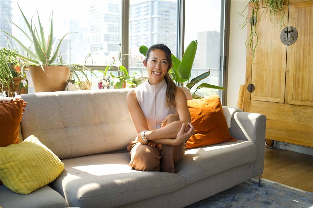 Steph Ngan seated on a couch, laughing, surrounded by plants