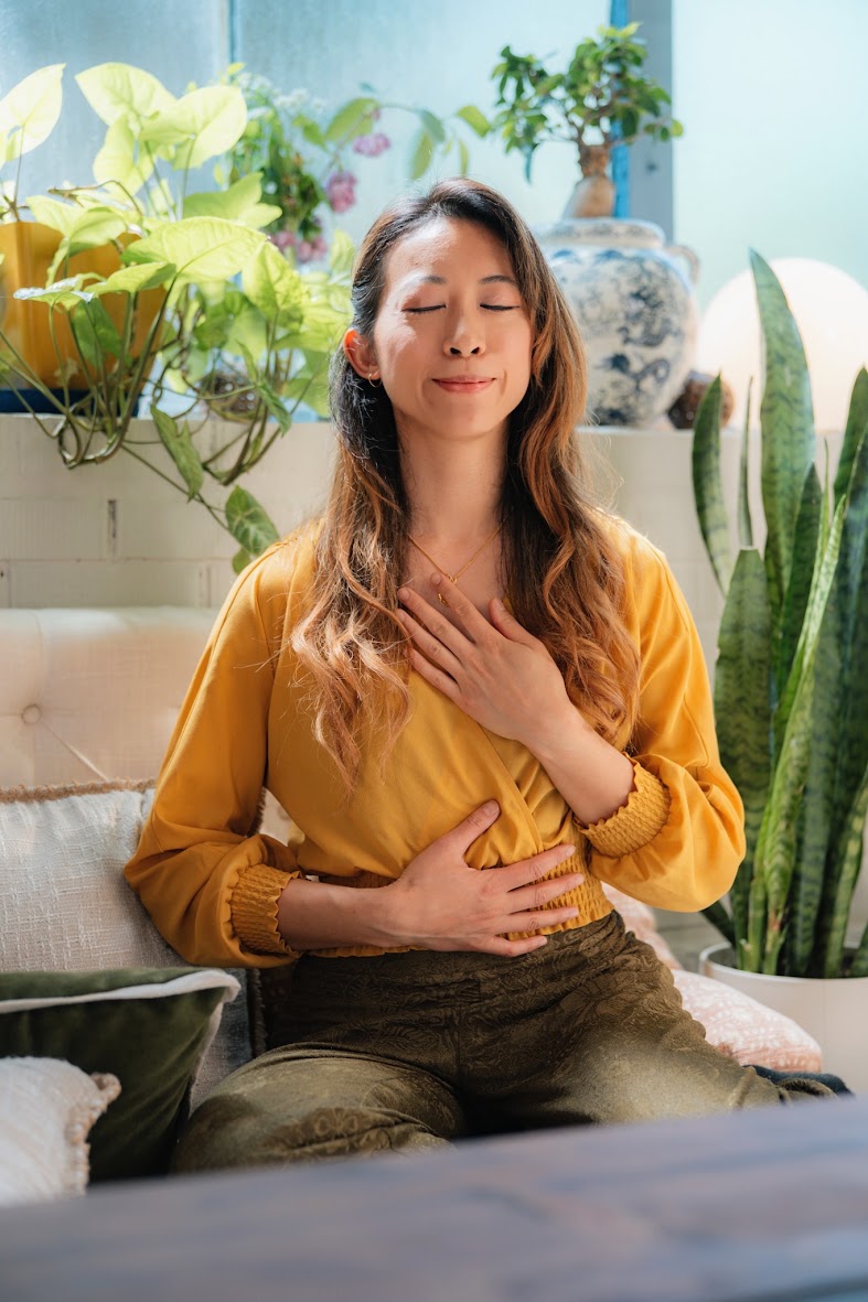 Steph Ngan seated with one hand on her chest and one on her stomach, eyes closed, breathing