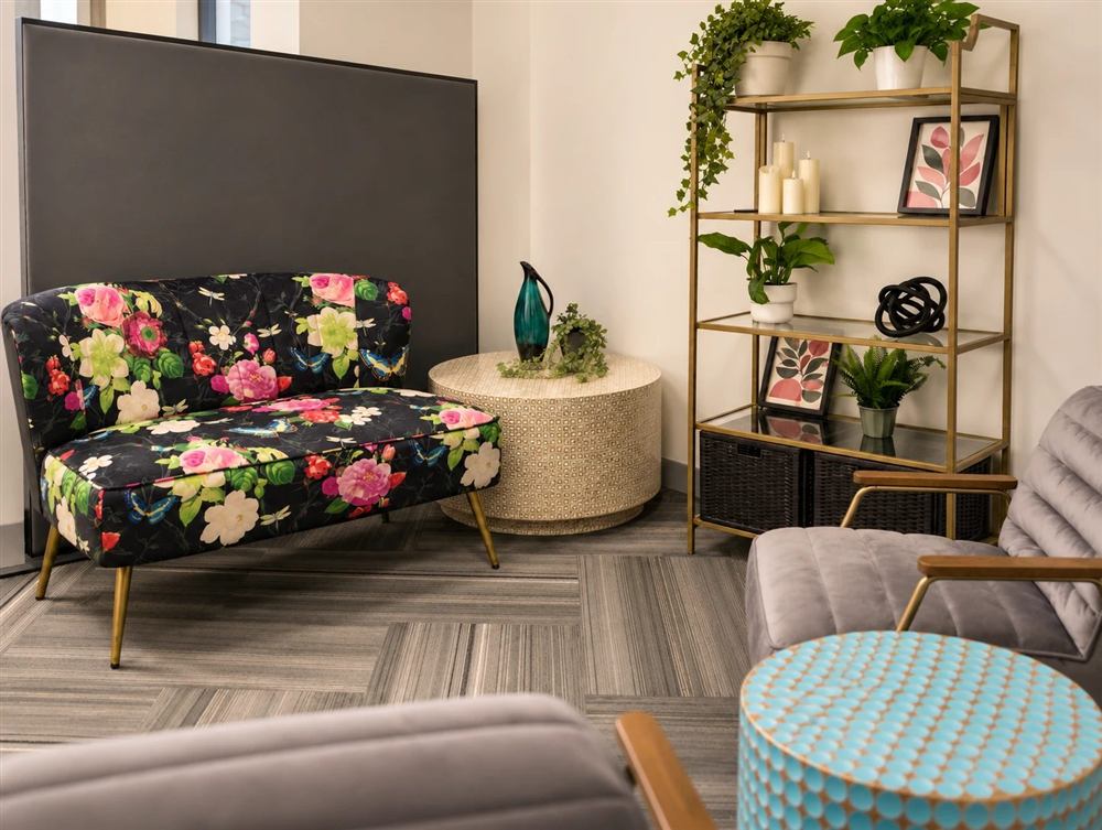 The therapy room, with a floral loveseat, a round side table, plants, and grey velvet armchairs